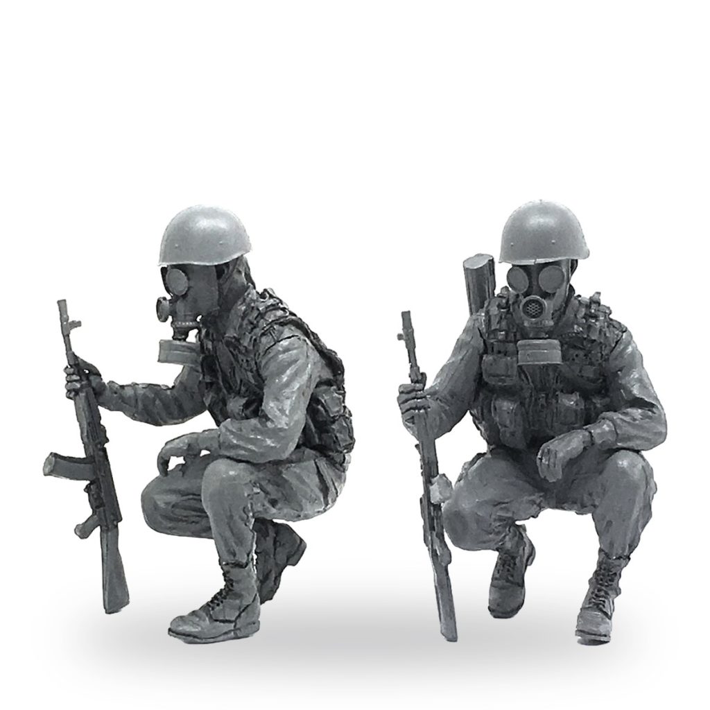 Two unpainted CBRN training soldier miniatures in crouching poses with rifles and gas masks.