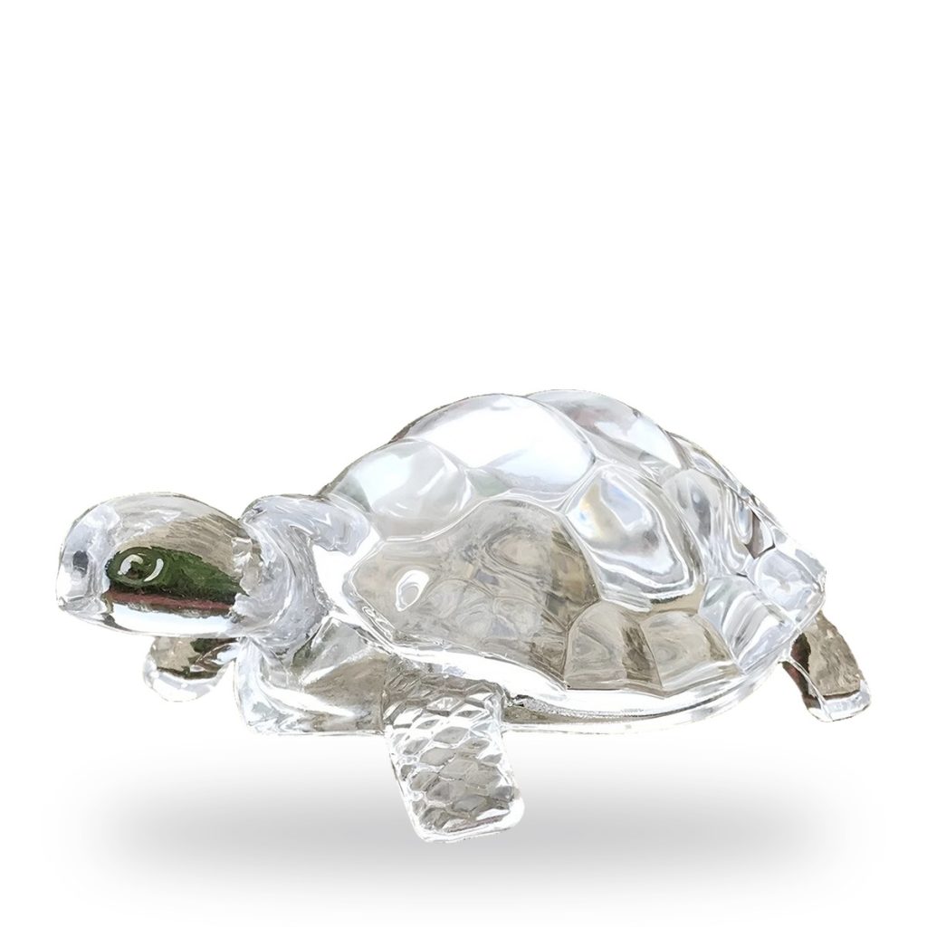 Unpainted glass figurine of a tortoise in dynamic pose with shadow.